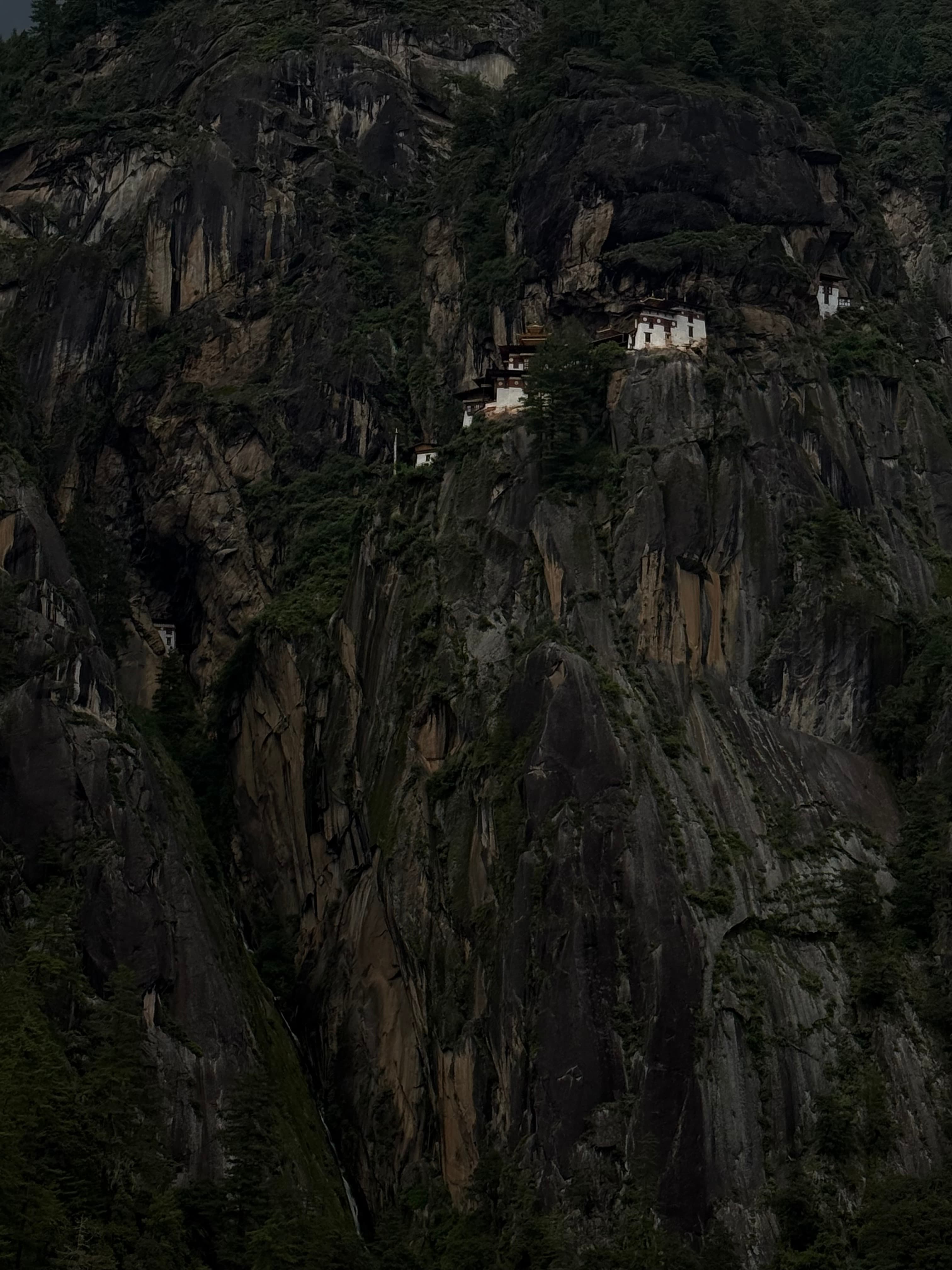 A monastery built into a dark cliff face, lit against the surrounding rock.
